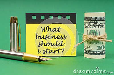 On a green surface, a pen, dollars, a notepad and yellow stickers with the inscription - What Business Should I Start Stock Photo