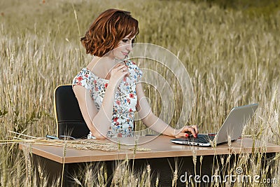 Business concept shot of a beautiful young woman sitting at a desk using a computer in a field. Stock Photo