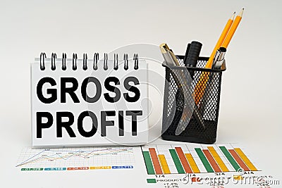 On the table are business charts, office supplies and a notepad with the inscription - gross profit Stock Photo