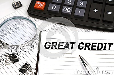 On the table is a magnifying glass, a calculator, a pen and a notebook with the inscription - Great Credit Stock Photo