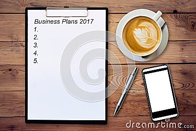 Business concept - Top view clipboard writing Business Plans 2017, pen, coffee cup, and phone on wood table. Stock Photo