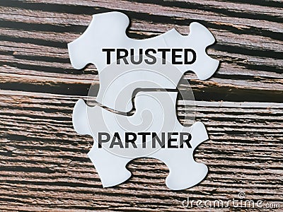 White jigsaw puzzles written trusted partner isolated on wooden background. Stock Photo