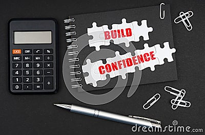 On the table is a calculator, a pen and a notebook with the inscription - Build Confidence Stock Photo