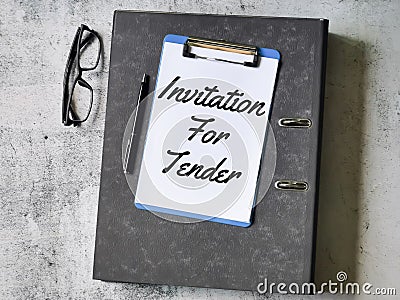 Selective focus paper clipboard written invitation for tender with pen,ring file and eye glasses. Stock Photo
