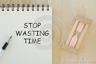 Business and finance concept. Top view of sand clock pen and notebook written with Stop Wasting Time. Stock Photo
