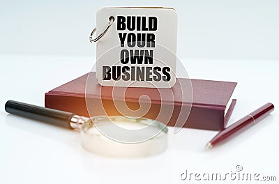 On the table there is a notebook, a pen, a magnifying glass and a notebook with the inscription Build your own business Stock Photo