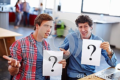 Business is full of questions. Portrait of two coworkers looking confused while holding question mark signs. Stock Photo