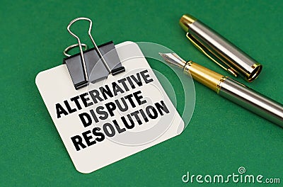 On a green surface, a pen and a sheet of paper with the inscription - Alternative Dispute Resolution Stock Photo