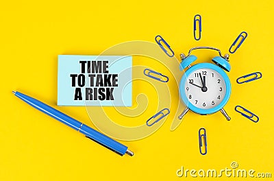 On the yellow surface there is an alarm clock, a pen and stickers with the inscription - Time to Take a Risk Stock Photo