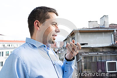 Business man with blue shirt using voice recognition in smart phone in the balcony Stock Photo