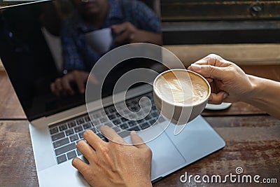 Business man holding coffee cup and typing on laptop computer keyboard on wooden table. Close up male hands with notebook pc Stock Photo