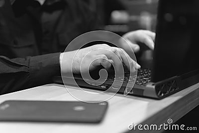 Business man with the laptop uses a mobile communication in cafe. Night time view from the street. Dark theme, in black style. Guy Stock Photo