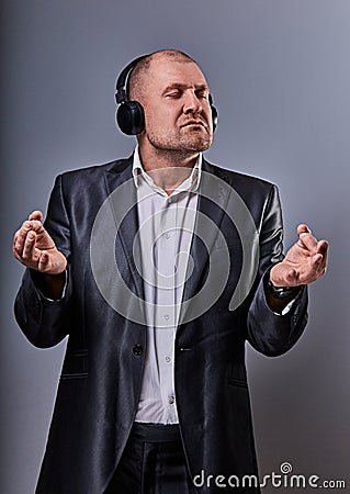 Business man listening the music in wireless earphone and trying relax he showing the hands yoga sign zen on grey studio Stock Photo