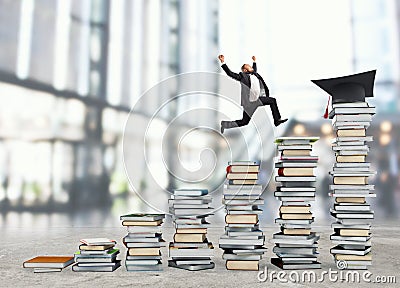 Business man reaches the graduation hat jumping on piles of books. Concept of success and determination on study Stock Photo