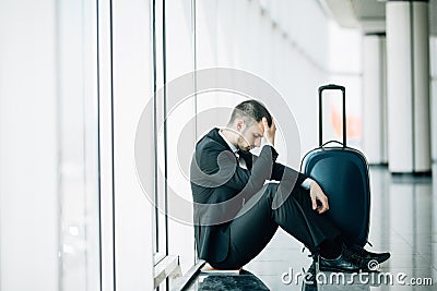 Business man sitting at the terminal airport on the floor with suitcase flight delay, two hands touch at head, headache, waiting t Stock Photo