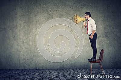 Business man standing on a chair and screaming into a megaphone Stock Photo