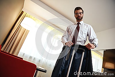 Business man takes his jacket to a suitcase near sofa at hotel room Stock Photo