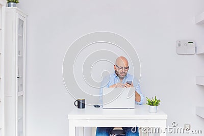 Business man teleworking from home with a laptop sending a message with his cell phone Stock Photo