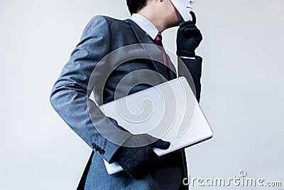 Business man in white mask wearing gloves and stealing computer and digital information - fraud, hacker, theft, cyber crime Stock Photo