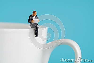 Business miniature figures sitting and read a book, read newspaper, waiting, talking and relax on white cup of hot coffee Stock Photo