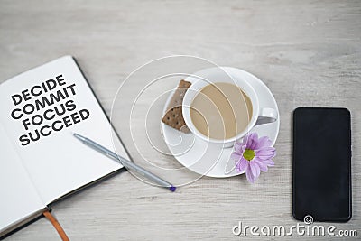 Business motivational words - Decide commit focus succeed. Written on open book with pen, cup of coffee with purple flower Stock Photo