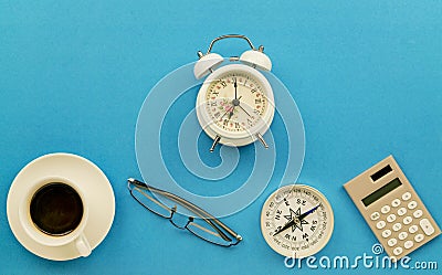 Business office table with business objects of white coffee cup,glasses,compass,calculator and vintage white alarm clock on blue Stock Photo
