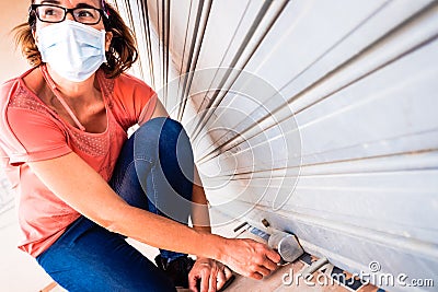 A business owner closes her business definitively by lowering the metal blind due to the economic crisis Stock Photo