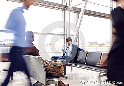 Business Passengers Sitting In Busy Airport Departure Lounge Using Mobile Phones Stock Photo