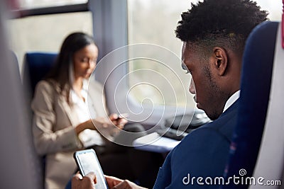 Business Passengers Sitting In Train Commuting To Work Looking At Mobile Phones Stock Photo