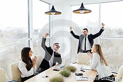 Business people in formalwear celebrate victory while sitting together at the table Stock Photo