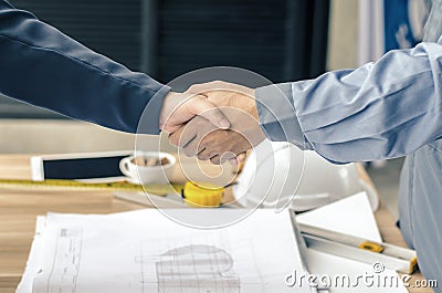 Business people handshaking at background over helmets, documents, worker tool Stock Photo