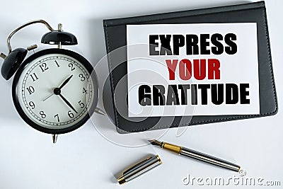 On the table there is a clock, a pen, a notebook and a card on which the text is written - EXPRESS YOUR GRATITUDE Stock Photo