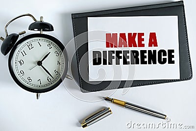 On the table there is a clock, a pen, a notebook and a card on which the text is written - MAKE A DIFFERENCE Stock Photo