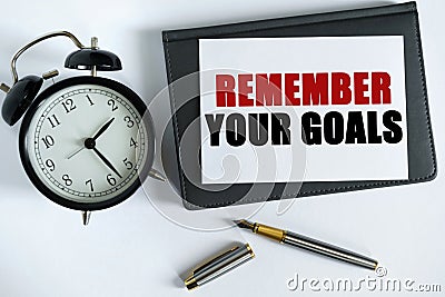 On the table there is a clock, a pen, a notebook and a card on which the text is written - REMEMBER YOUR GOALS Stock Photo