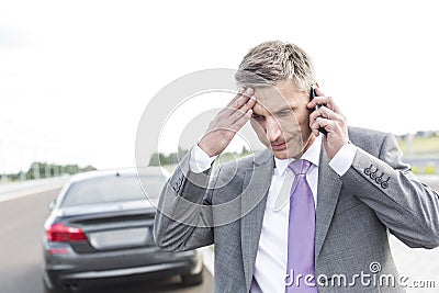 Tensed businessman talking on mobile phone against breakdown car Stock Photo