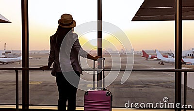 Business trip of young woman in hat which holding the luggage and looking the airplane in the hall room with sunlight in the Stock Photo
