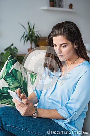 Business woman in blue shirt chatting,talking in mobile phone.Remote work at home office sitting on couch.Messaging,dating,meeting Stock Photo