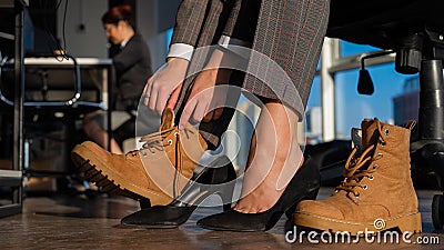 Business woman changes shoes with high heels on boots in the office. End of the working day. Tired legs Stock Photo