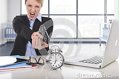Business woman furious and angry working with computer laptop pointing gun to alarm clock Stock Photo