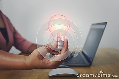 business woman hand holding light bulb with using laptop in office. concept saving energy power Stock Photo