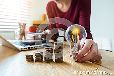 Business woman hand holding lightbulb with coins stack on desk. concept saving energy. Stock Photo