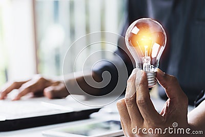 Business woman holding light bulb on the desk in office and using computer in financial,accounting,energy,idea concept Stock Photo