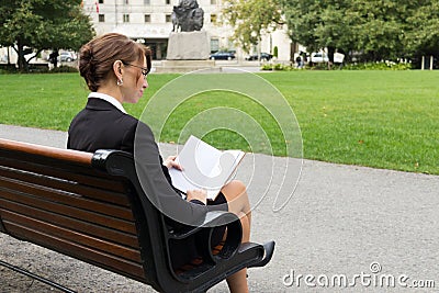 Business woman reads while sitting on park bench Stock Photo