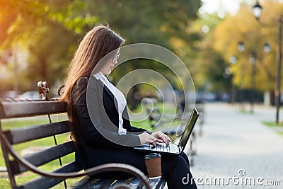 Business woman sitting in the park on a bench, working with a laptop Stock Photo