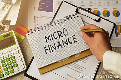 Business woman at the table in the office makes notes in a notebook. The inscription MICRO FINANCE is important for promoting your Stock Photo