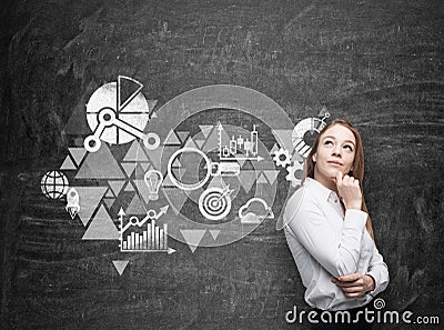 Business woman is thinking about business optimisation scheme. Black chalk board as a wall on the background. Stock Photo