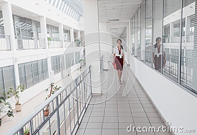 Business Woman Walking Along the Office Corridor. Smiling Businesswoman Goes Against White Offices Background. A young pretty girl Stock Photo