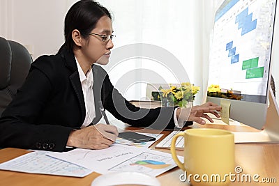 Business woman working in office looking and check paper note. business people analysis scheduler data on PC screen. Business Stock Photo