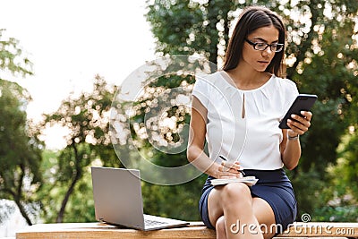 Business woman writing notes chatting by mobile phone Stock Photo