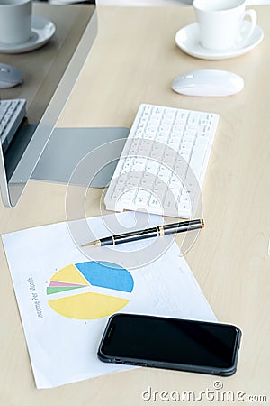 Business workplace concept. Cup of hot coffee on work desk with computer keyboard Mobile and papers graphs Stock Photo